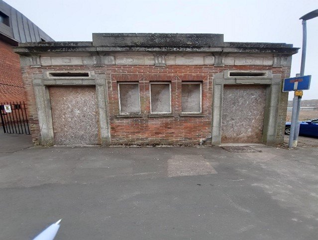 A picture of an old, derelict and boarded-up public toilet building.