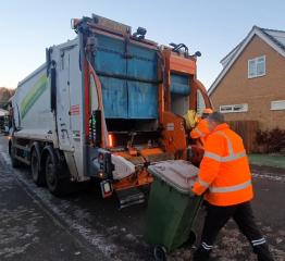 A waste collection operative wheeling a garden waste bin towards the collection vehicle in frosty weather